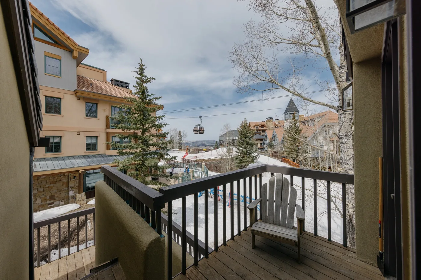 A balcony overlooks snow-covered buildings and a gondola beneath a cloudy sky.