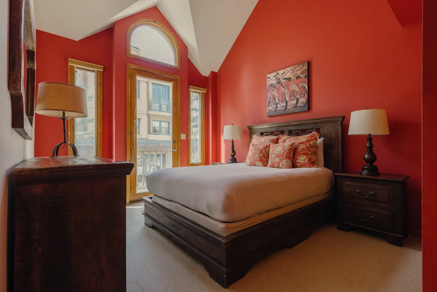 A bedroom with a large bed, red walls, and tall windows.