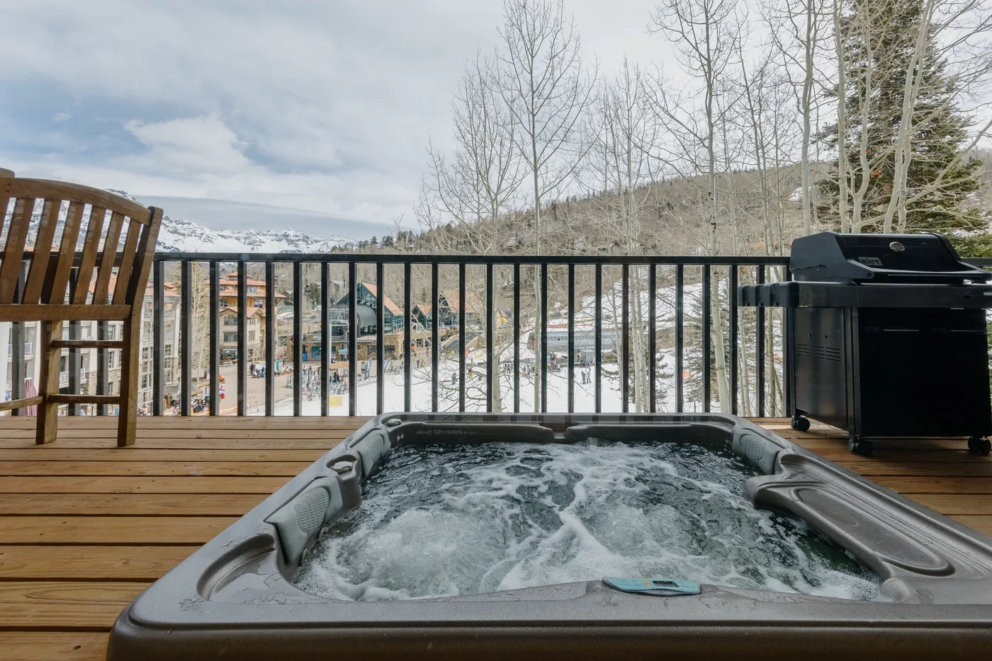 An outdoor hot tub sits on a wooden deck overlooking a snow-covered town.