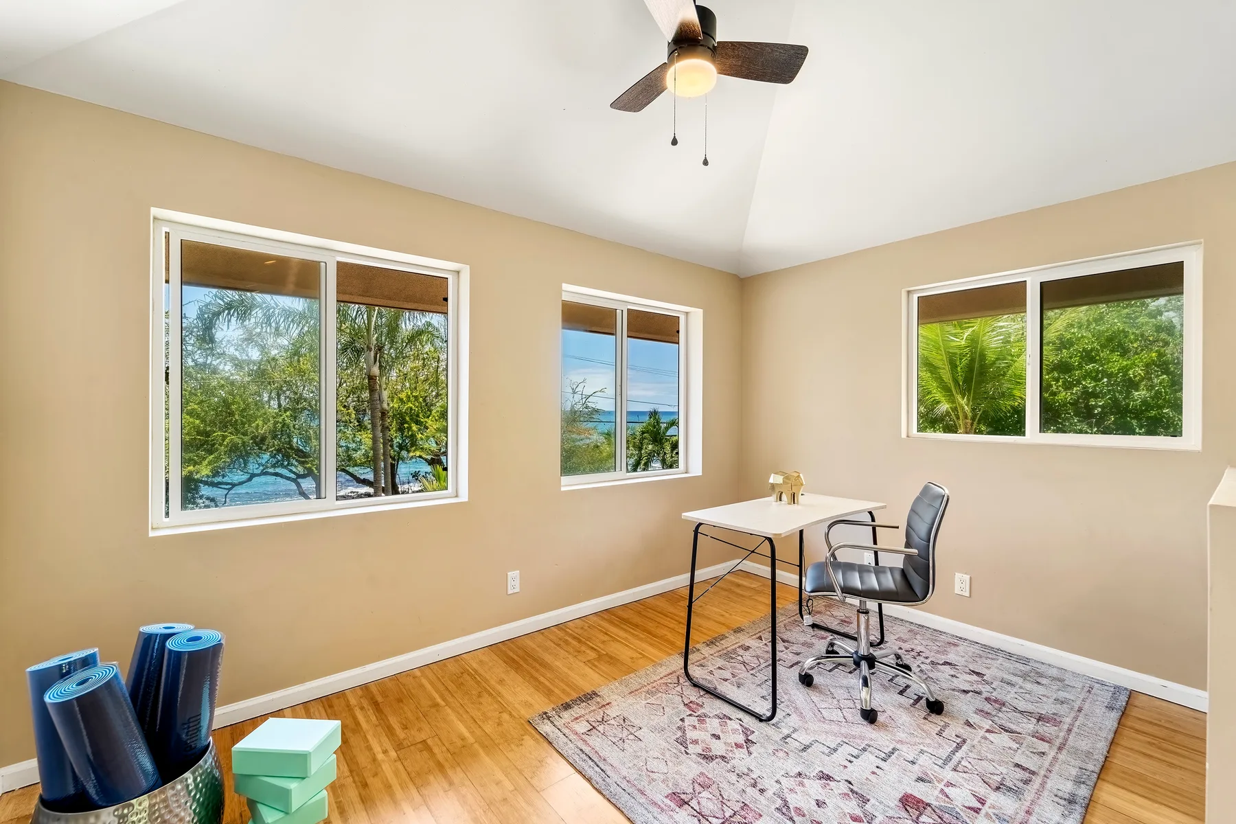 Una habitación luminosa con escritorio y silla junto a ventanas con vistas a la vegetación.