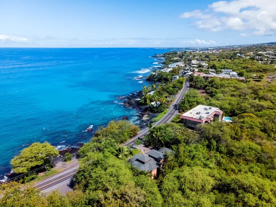 Vista aérea de una carretera costera junto a aguas turquesas y vegetación verde.