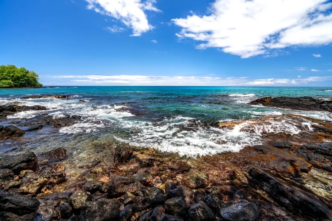 Una costa rocosa se encuentra con aguas claras bajo un cielo parcialmente nublado.