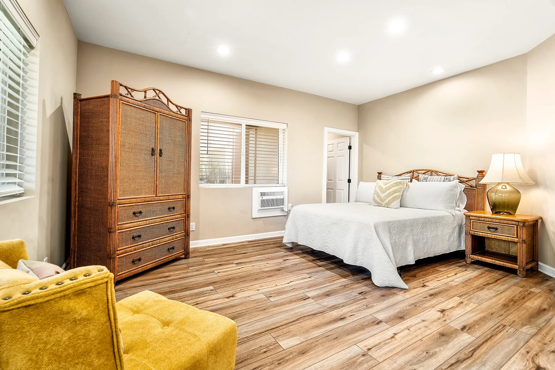 Un dormitorio luminoso con una cama, una cómoda de madera y asientos amarillos.