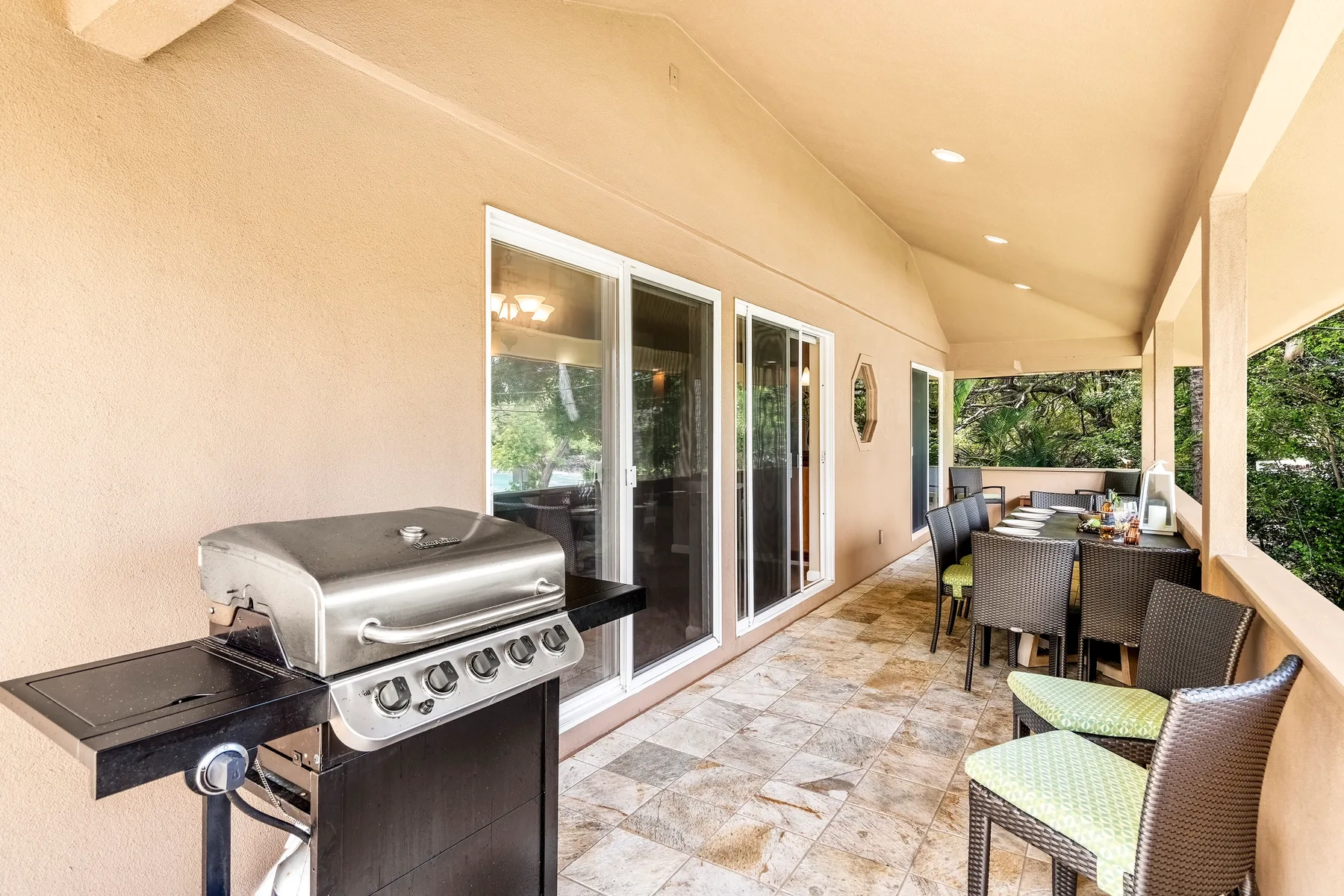 Un patio cubierto con una parrilla y una mesa de comedor junto a puertas de vidrio.