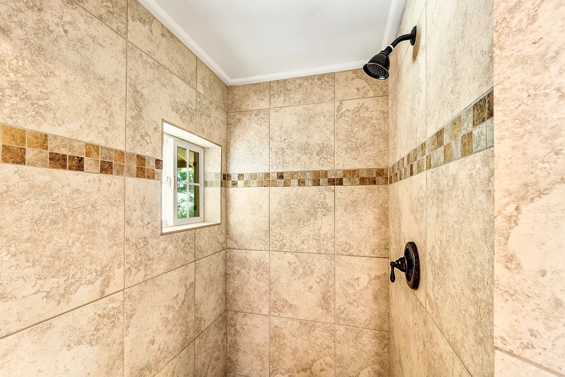 Una ducha con azulejos, una ventana pequeña y accesorios oscuros.