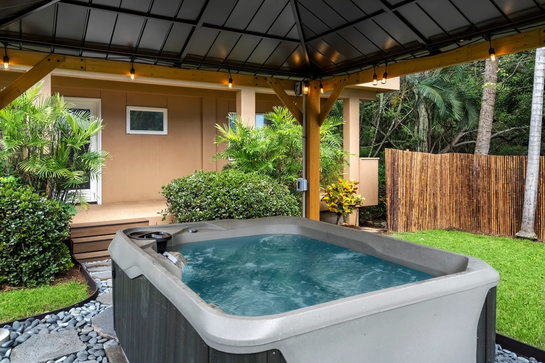 Una bañera de hidromasaje exterior cubierta está junto a un jardín ajardinado.