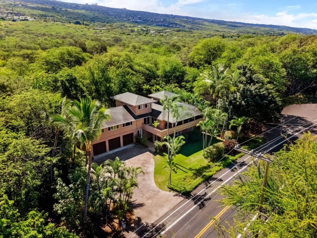 Una casa grande está junto a una carretera pavimentada, rodeada de abundante vegetación.
