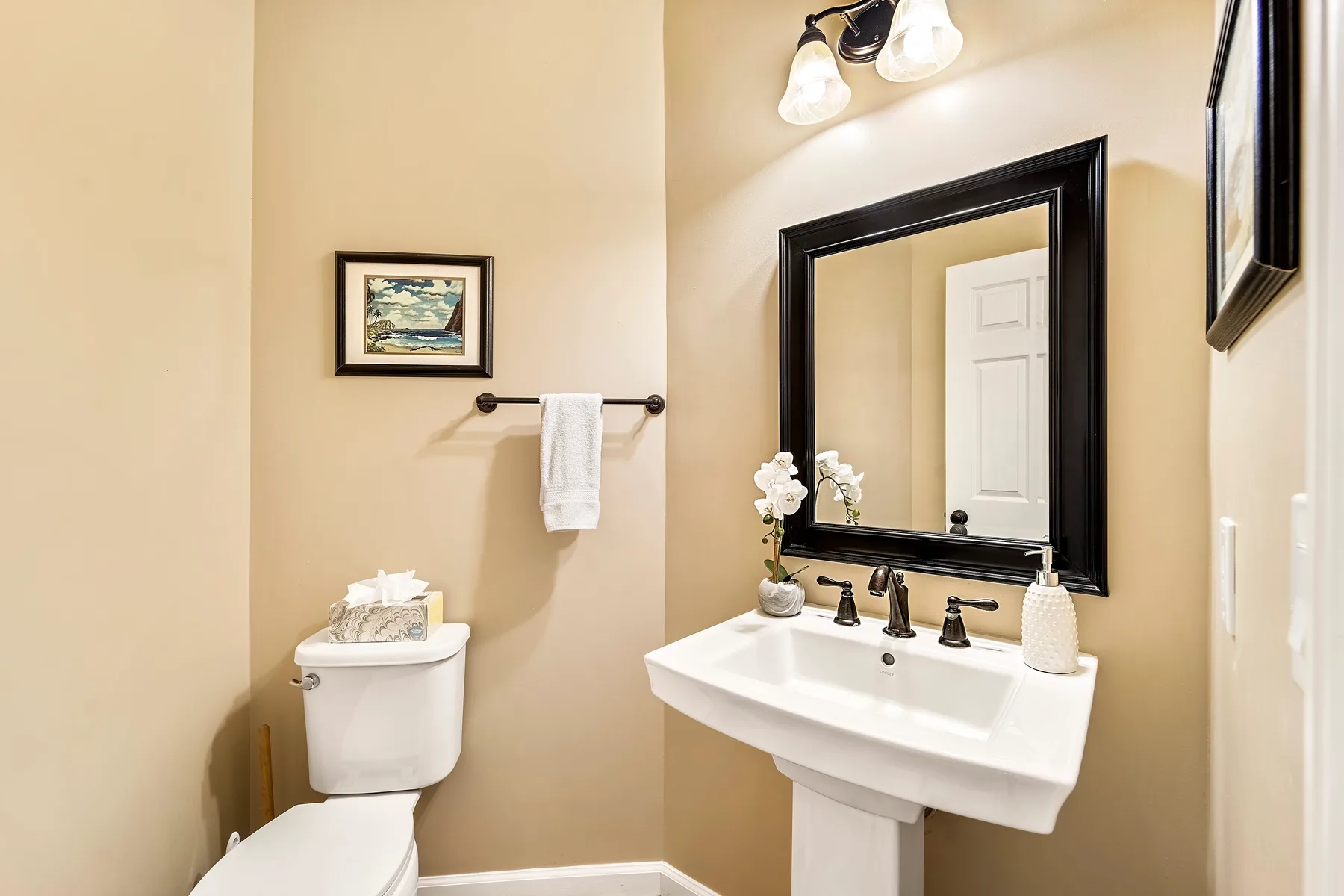 Un lavabo de baño con espejo, junto a un inodoro y un toallero.