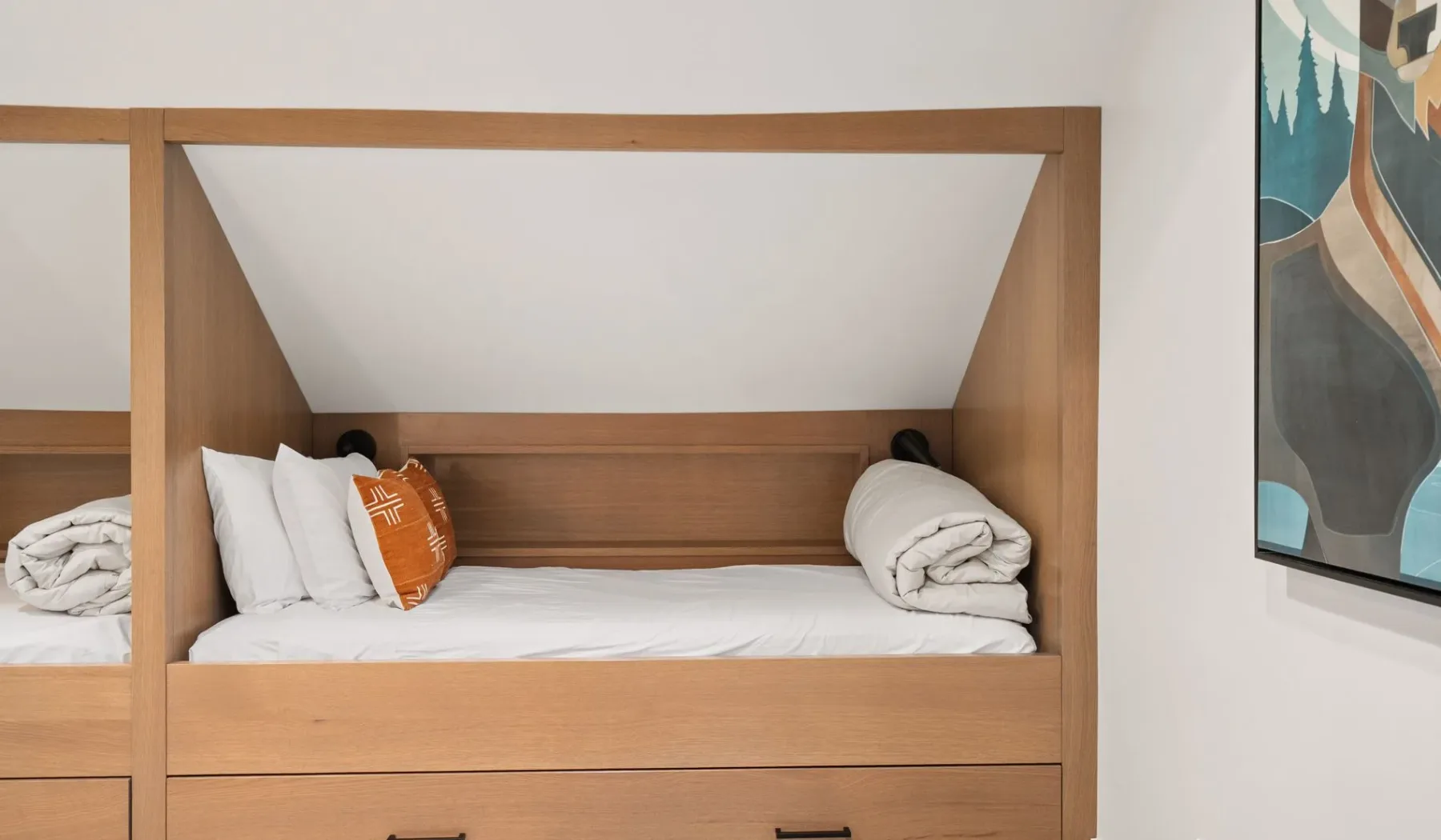 Una litera de madera con ropa de cama blanca y un cojín naranja.