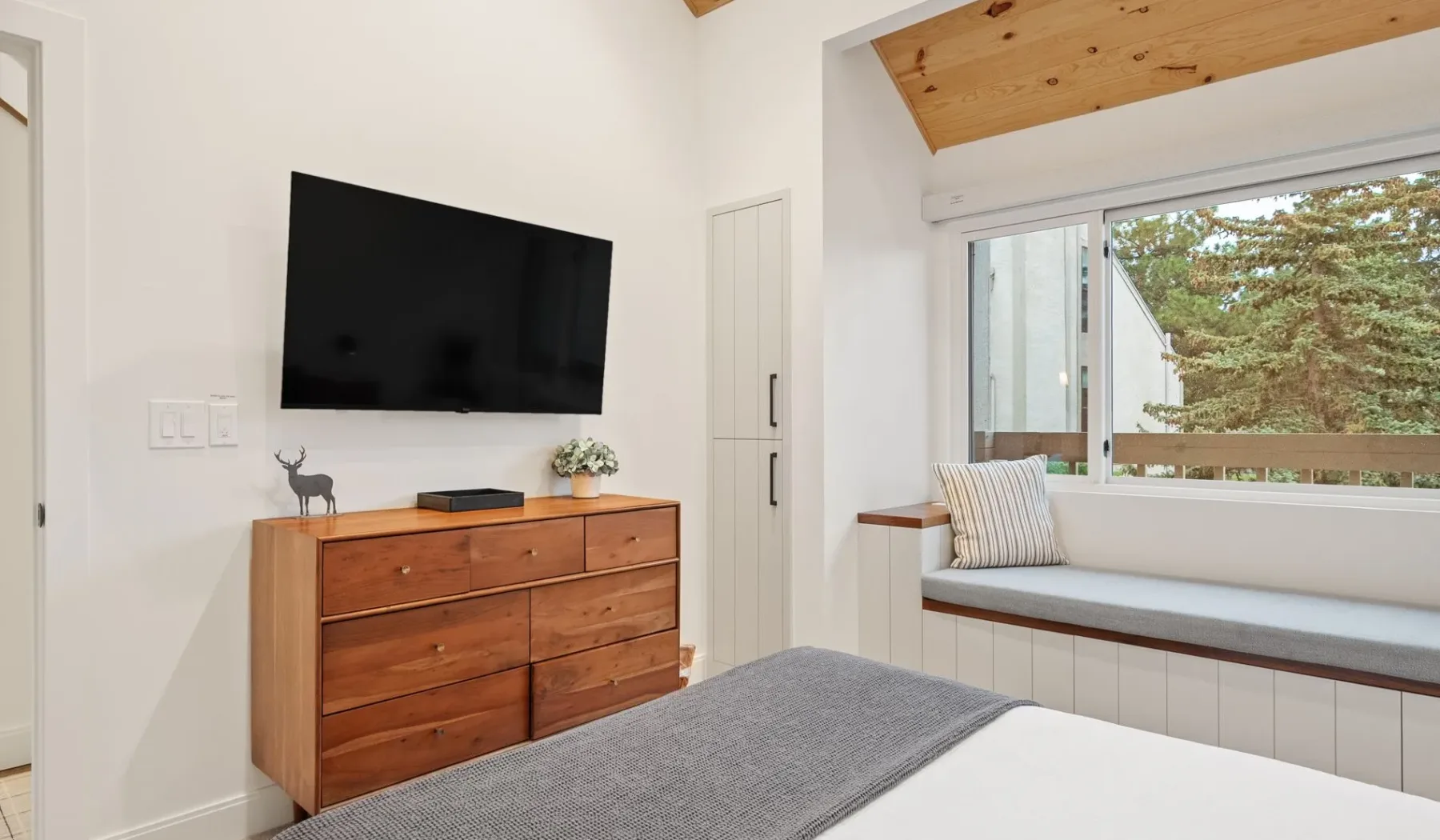 Un dormitorio luminoso con cama, cómoda de madera y banco junto a la ventana.