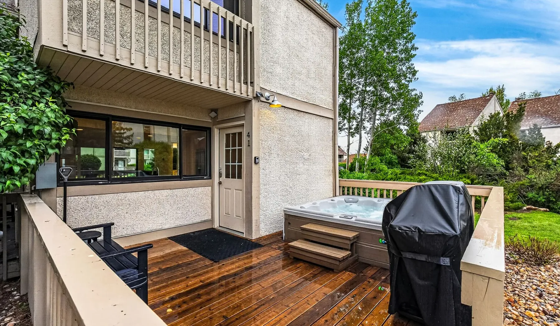 Una terraza exterior con una bañera de hidromasaje y una parrilla cubierta junto a la casa.
