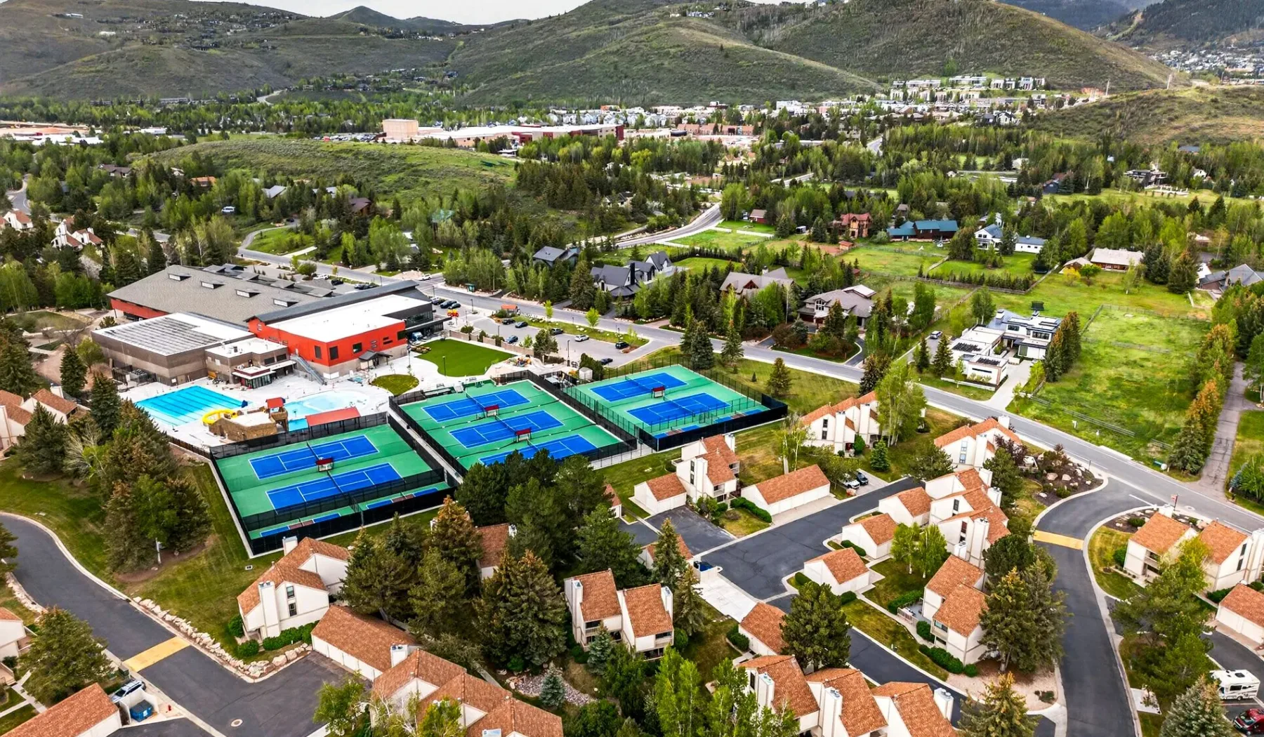 Vista aérea de un barrio residencial junto a pistas de tenis y una piscina.
