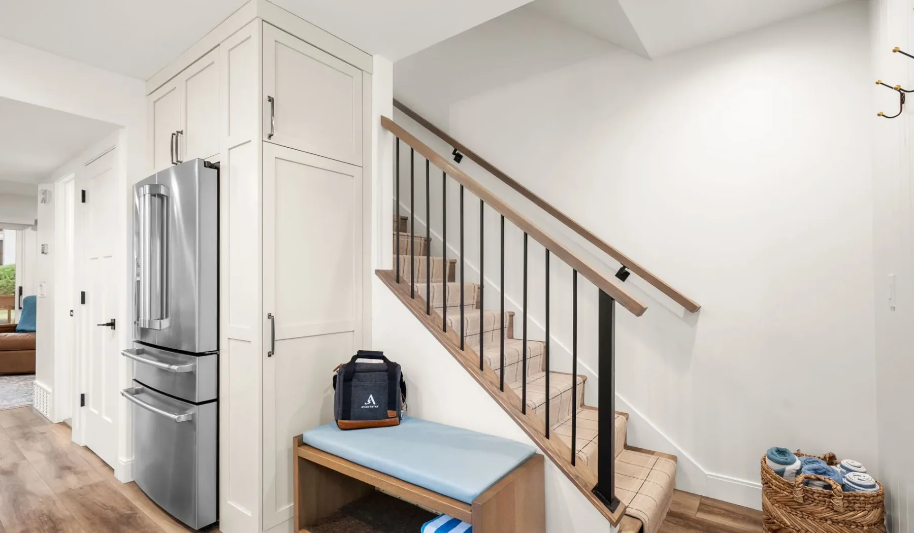 Una entrada luminosa con una escalera, un refrigerador y un banco.