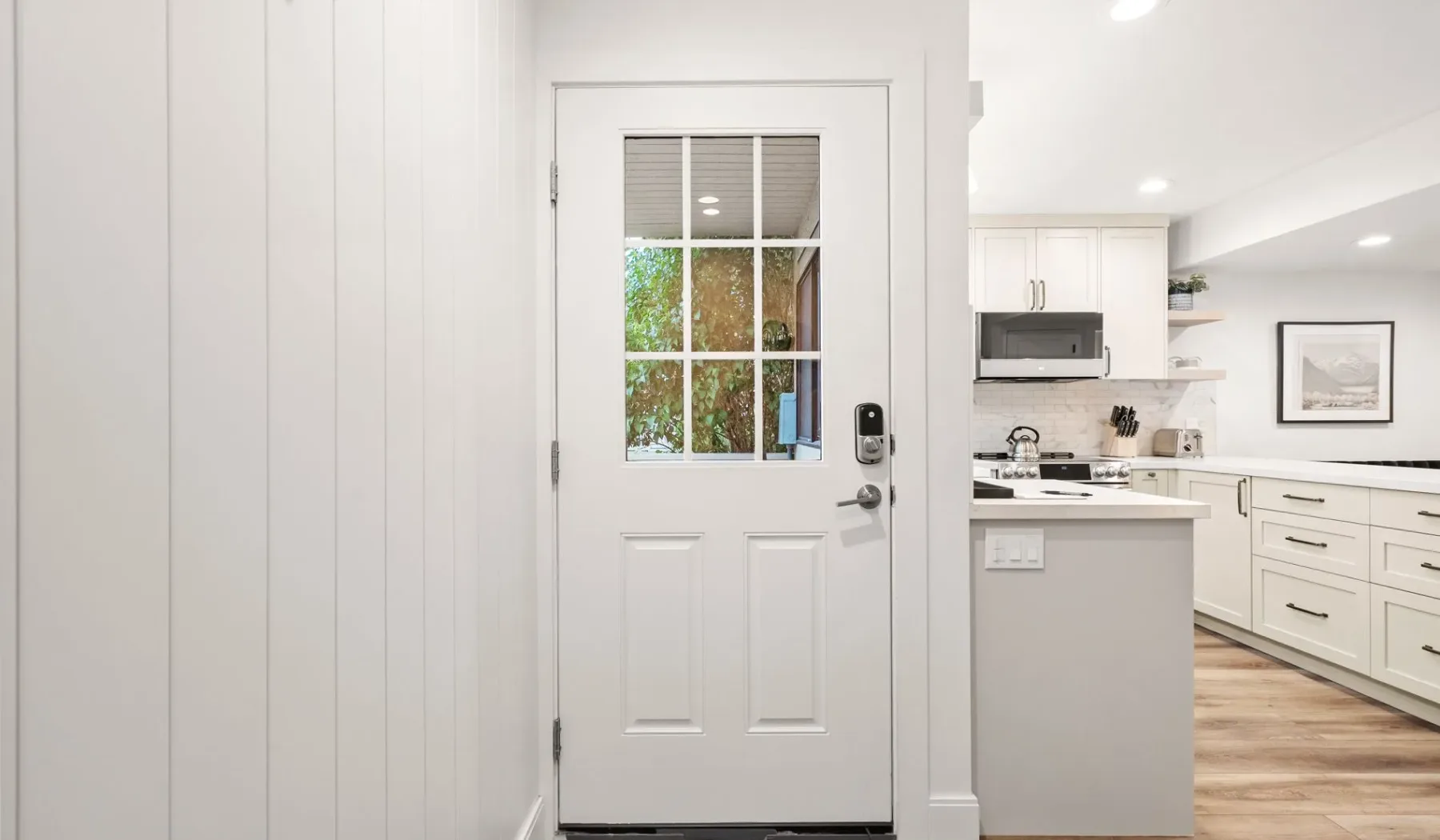 Una puerta blanca da a una cocina luminosa con gabinetes claros.