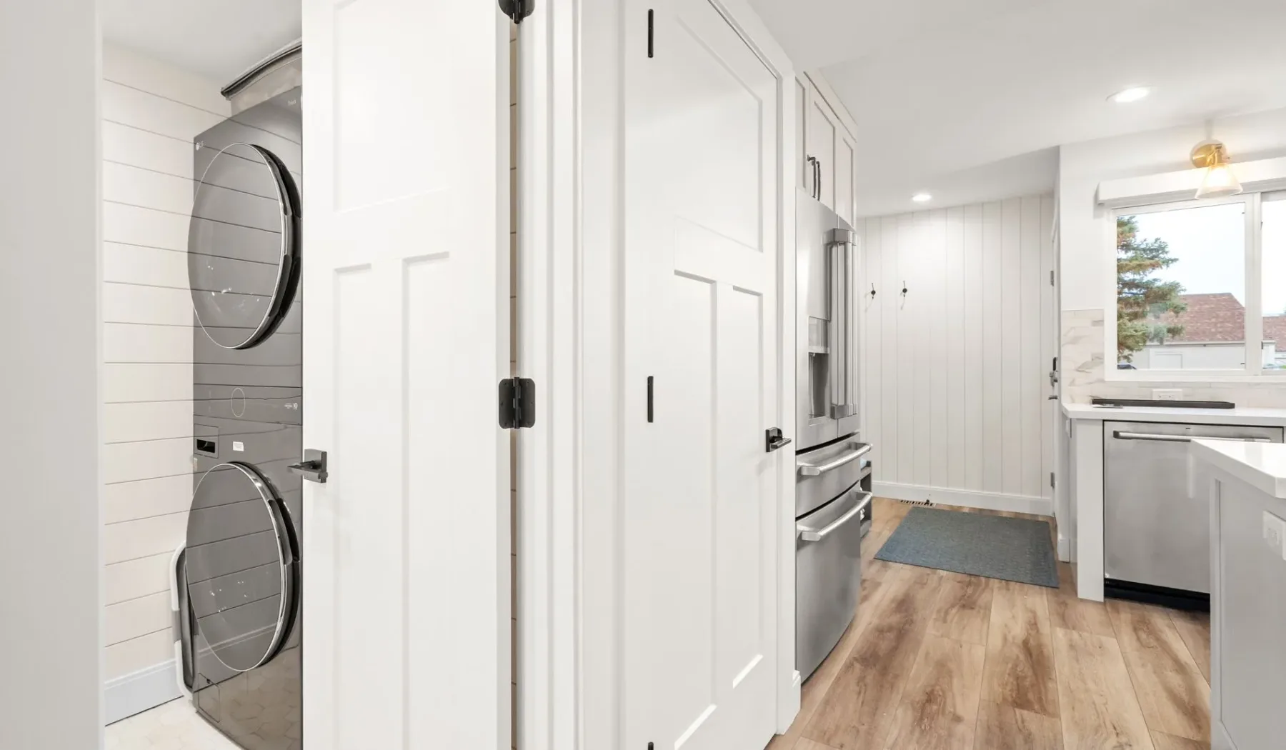 Una cocina luminosa con electrodomésticos de acero inoxidable, gabinetes blancos y piso imitación madera.