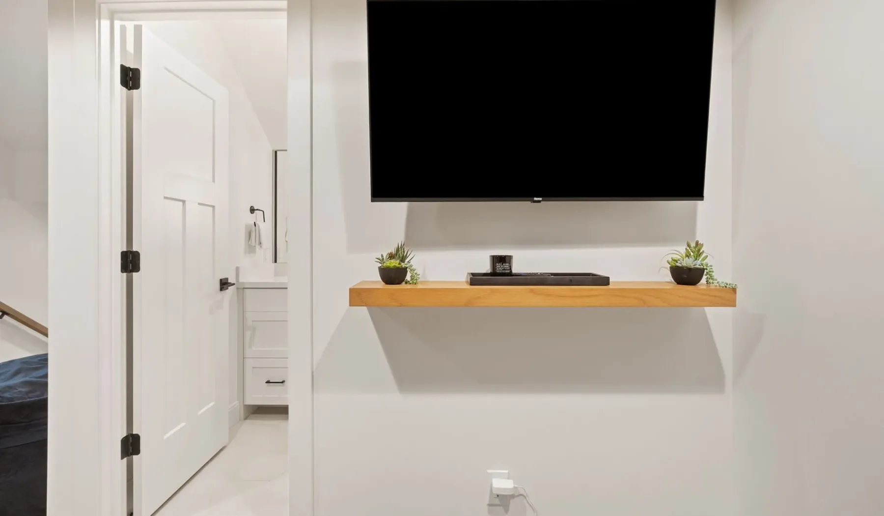Un televisor montado en la pared está sobre un estante de madera con plantas pequeñas.