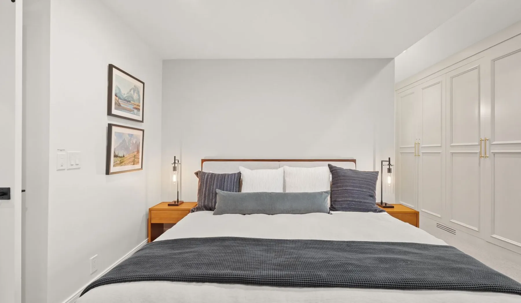 Un dormitorio con una cama bien arreglada y cuadros en la pared.
