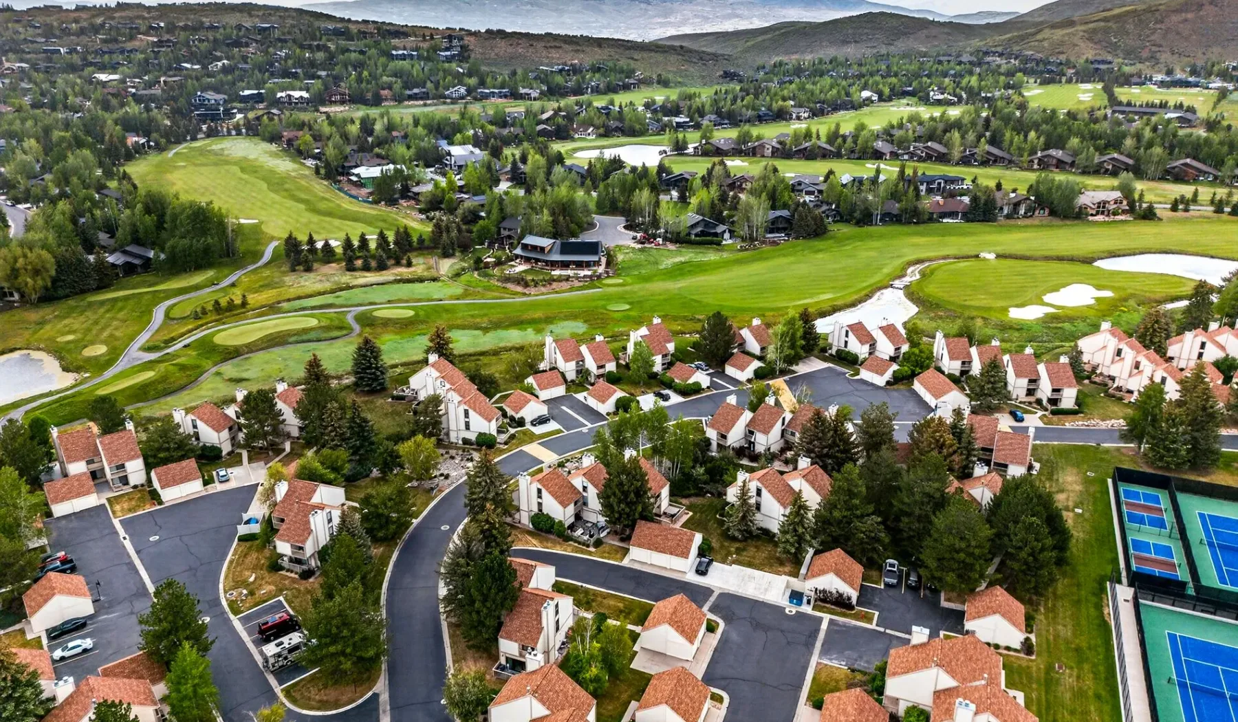 Vista aérea de un barrio residencial junto a un campo de golf y colinas verdes.
