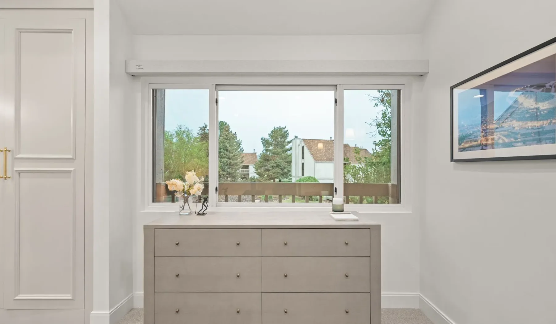 Un dormitorio luminoso con una ventana amplia sobre una cómoda baja.