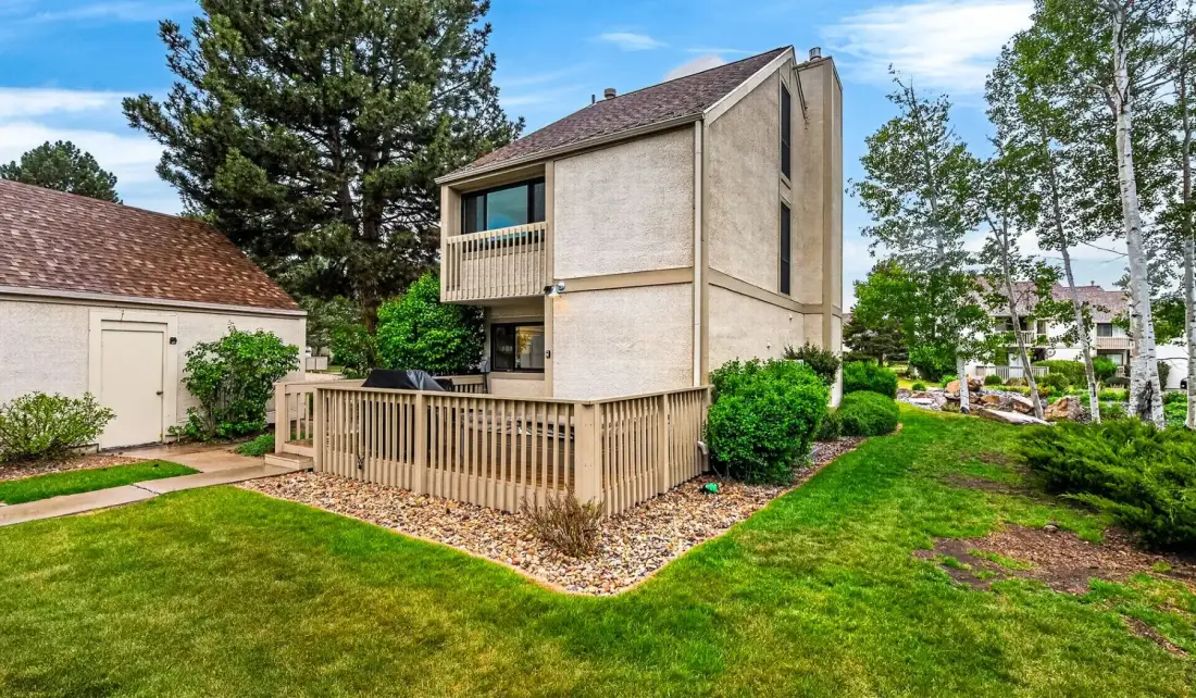 Un edificio de varios pisos con una terraza de madera está junto a un césped verde.