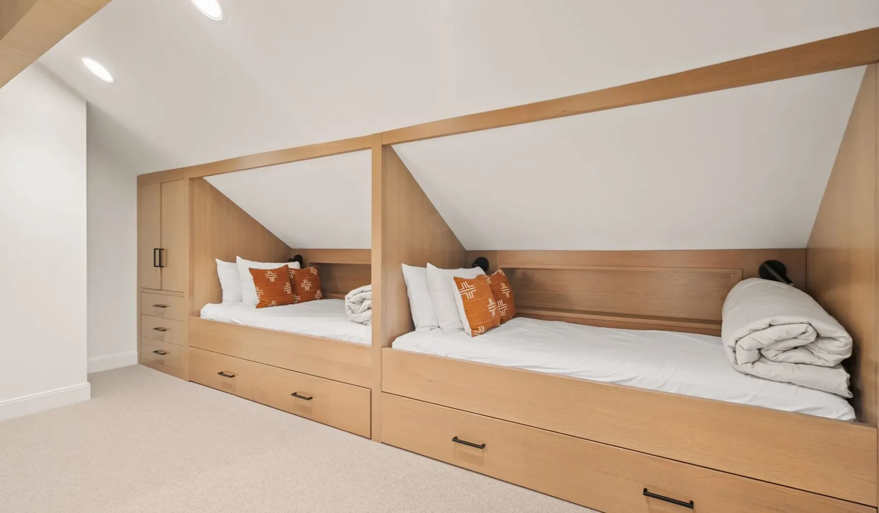 Un dormitorio con dos camas empotradas, ropa de cama blanca y cojines naranjas.