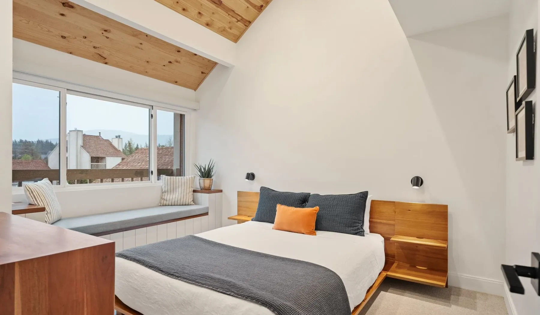 Un dormitorio luminoso con cama, asiento junto a la ventana y techo de madera.