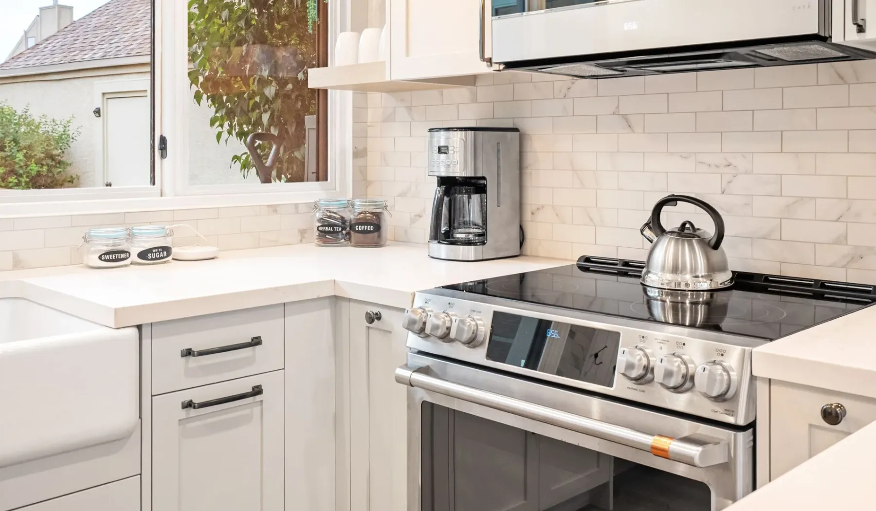 Una cocina luminosa con gabinetes blancos y una tetera sobre la estufa.