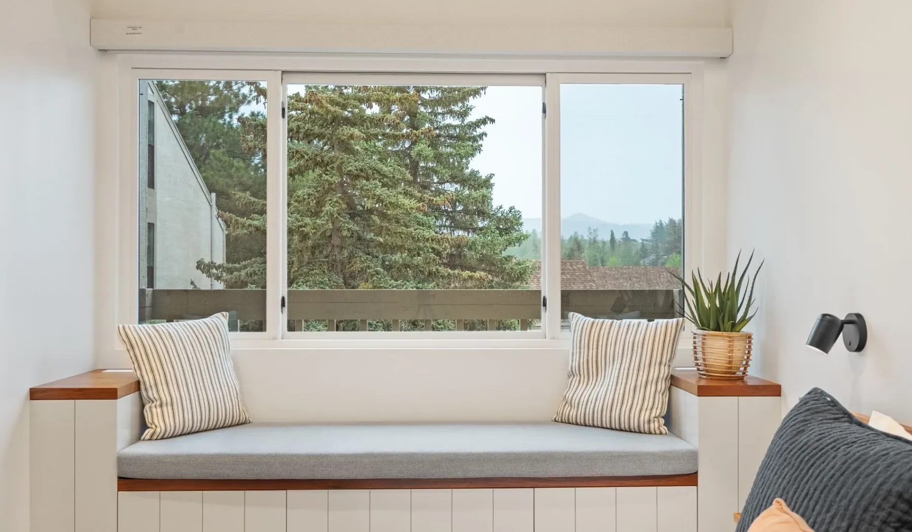 Una luminosa zona de descanso junto a la ventana, con cojines a rayas y vistas a los árboles.