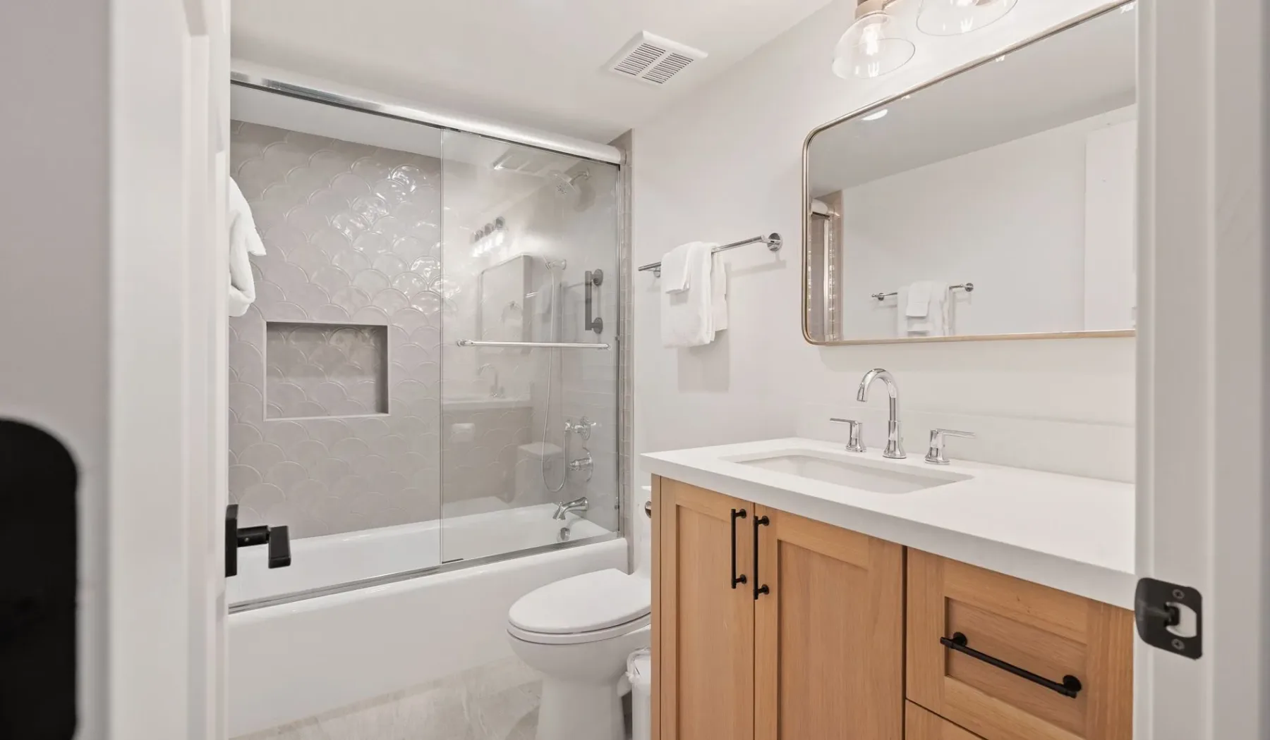 Un baño luminoso con ducha de vidrio, bañera y tocador de madera.