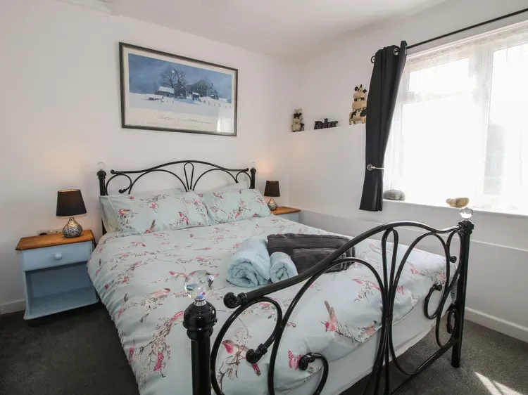Un dormitorio con una colcha floral, una estructura de cama metálica oscura y una ventana luminosa.