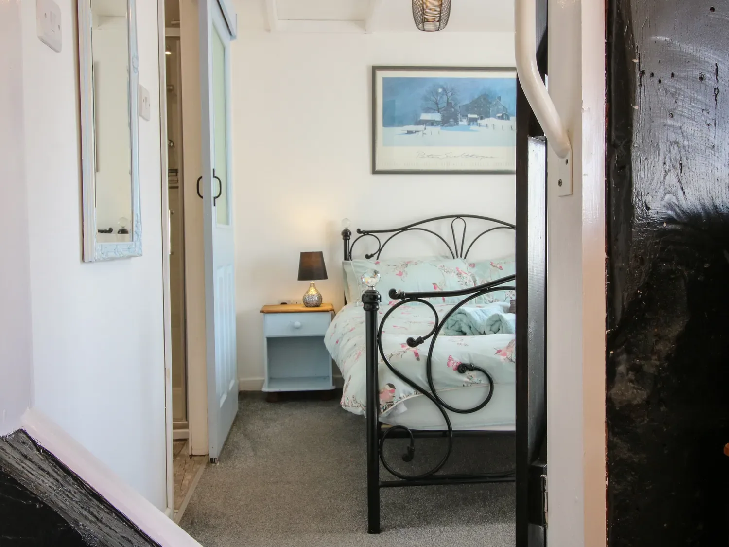 Un dormitorio con una estructura de cama de metal negro, una mesita de noche azul con una lámpara y un cuadro enmarcado en la pared en The Old Beams, en Pont y Forwyn, Llansantffraidd-ym-Mechain, cerca de Welshpool.