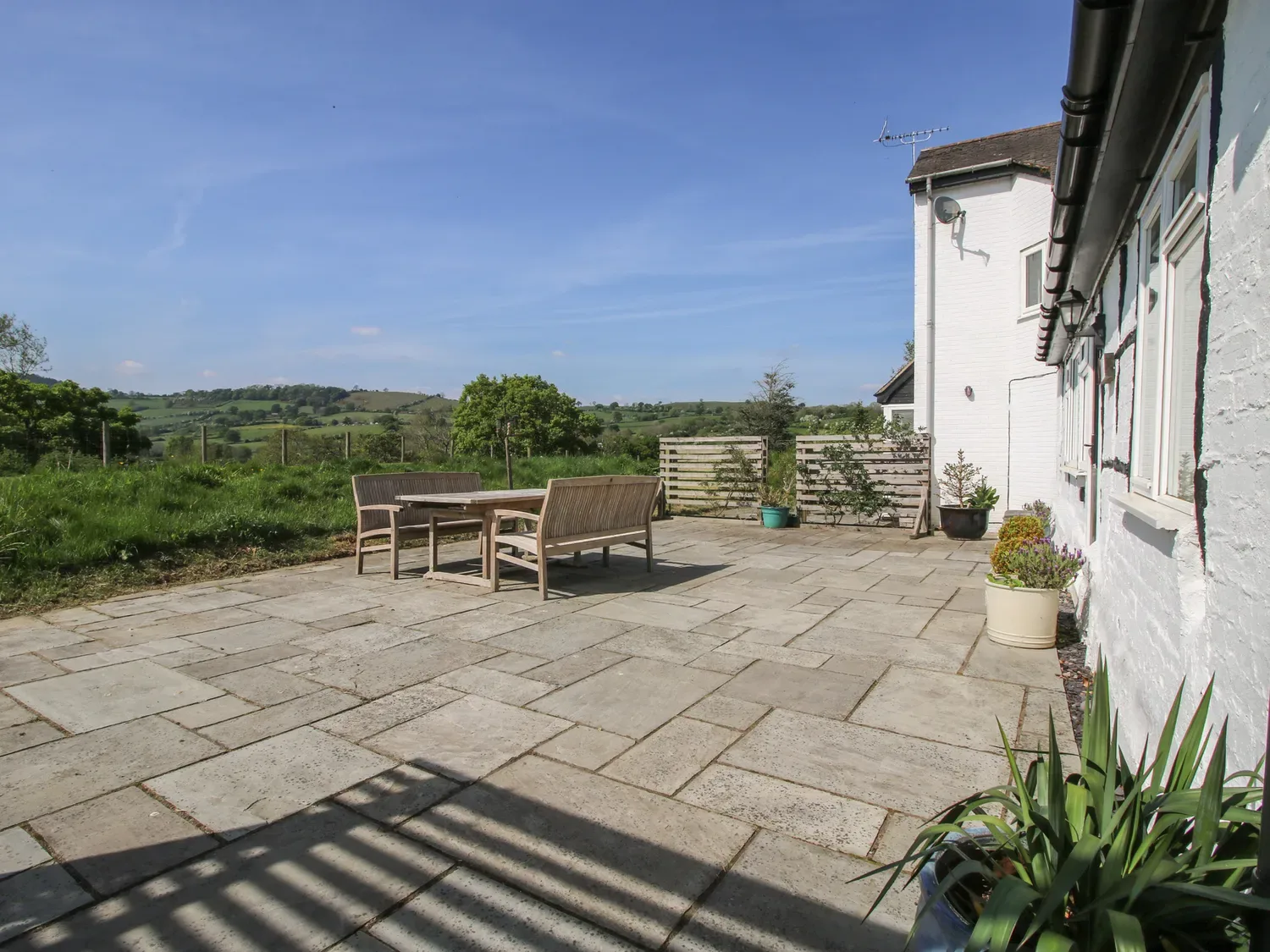 Una zona de patio exterior con mesa y sillas de madera y plantas en macetas junto a una casa blanca en The Old Beams, en Pont y Forwyn, Llansantffraidd-ym-Mechain, cerca de Welshpool.