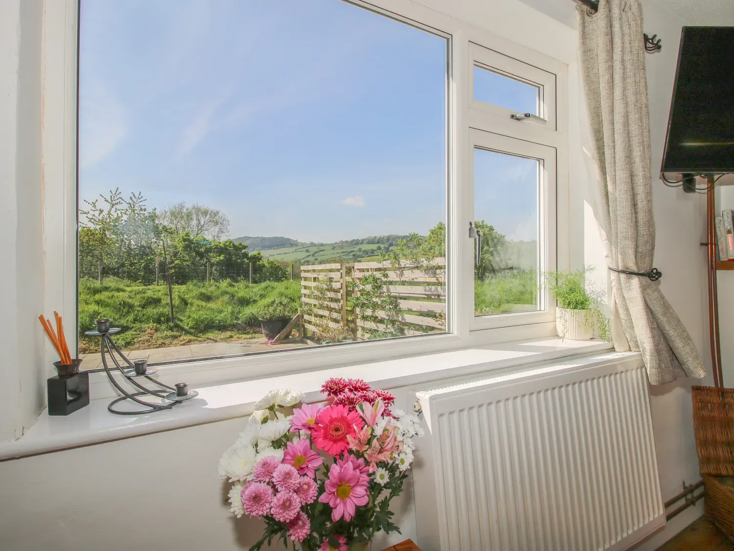 Una habitación luminosa tiene una ventana amplia con vistas a colinas verdes y un jardín.