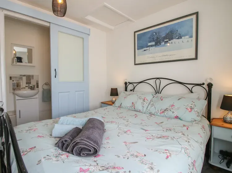 Un dormitorio con ropa de cama floral, mesillas y un cuadro enmarcado sobre la cama.