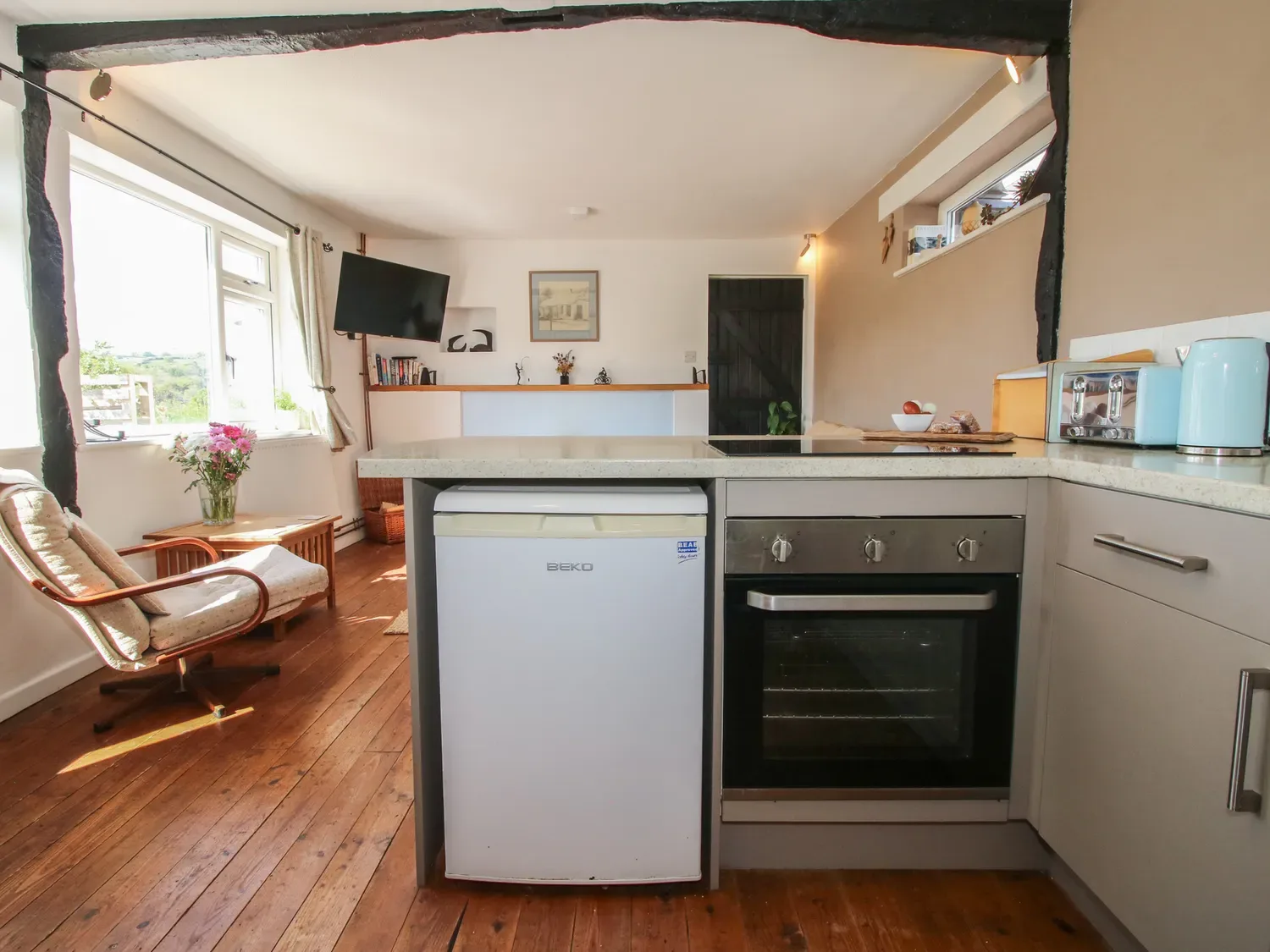 Una cocina con un frigorífico, un horno, una silla y flores junto a una ventana en The Old Beams, en Pont y Forwyn, Llansantffraidd-ym-Mechain, cerca de Welshpool.