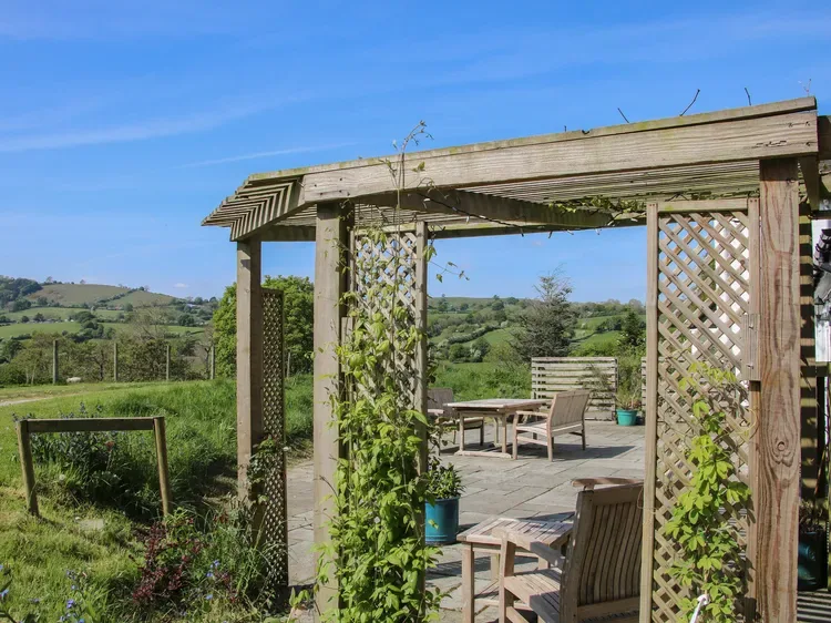 Una pérgola cubre una zona de estar al aire libre con vistas al campo verde.