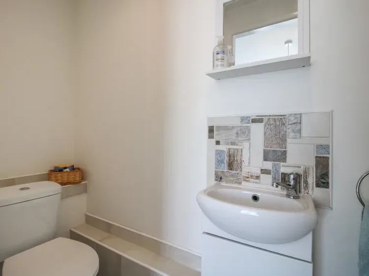 Un baño con un inodoro y un lavabo de pared debajo de una ventana pequeña.