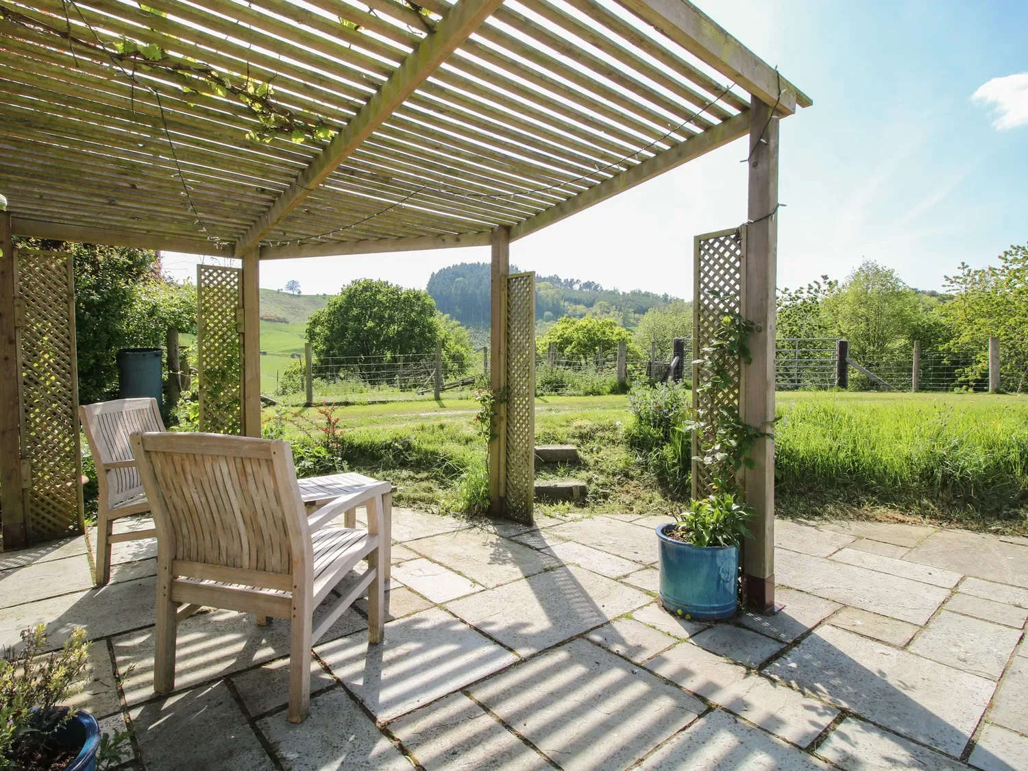 Un patio exterior con sillas de madera bajo una pérgola con vistas a un campo verde en The Old Beams, en Pont y Forwyn, Llansantffraidd-ym-Mechain, cerca de Welshpool.