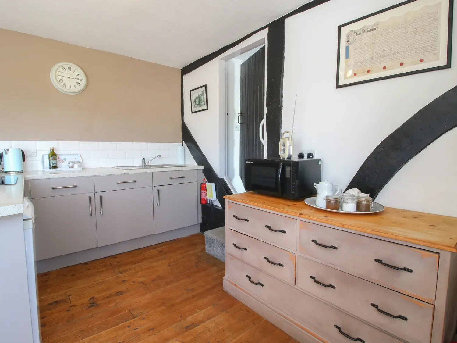 Una cocina con armarios, un microondas sobre un aparador y un reloj en la pared en The Old Beams, en Pont y Forwyn, Llansantffraidd-ym-Mechain, cerca de Welshpool.