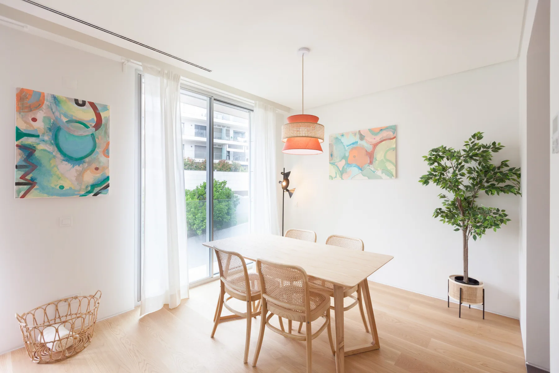 A bright dining area with a wooden table, woven seating, and colorful wall art.