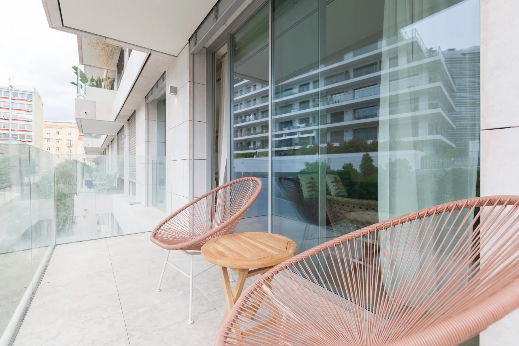 A balcony seating area with two woven chairs and a small wooden table.