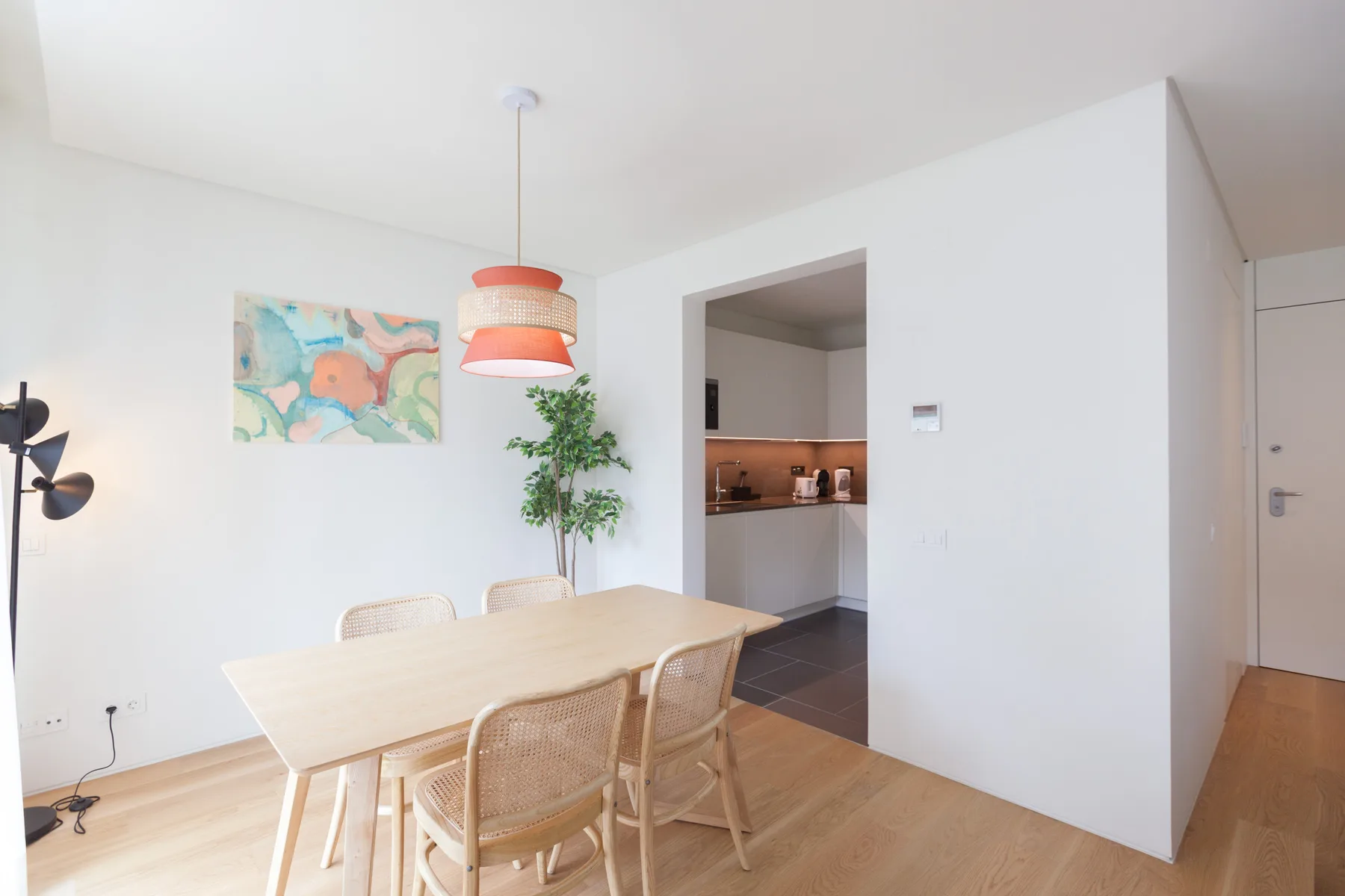 A bright dining area with a light wood table beside an open kitchen.