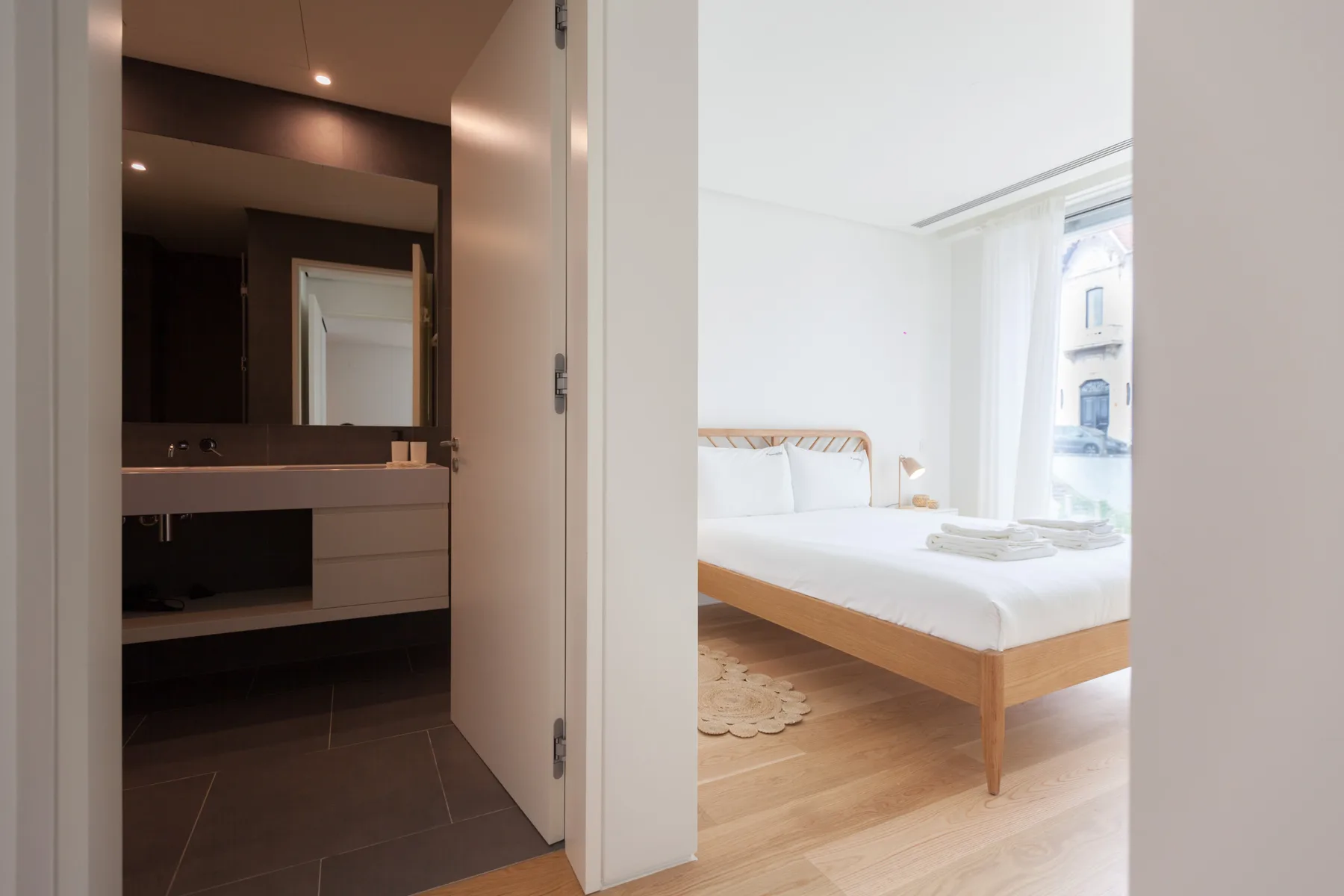 A bright bedroom with a wooden bed is visible beside an open bathroom.
