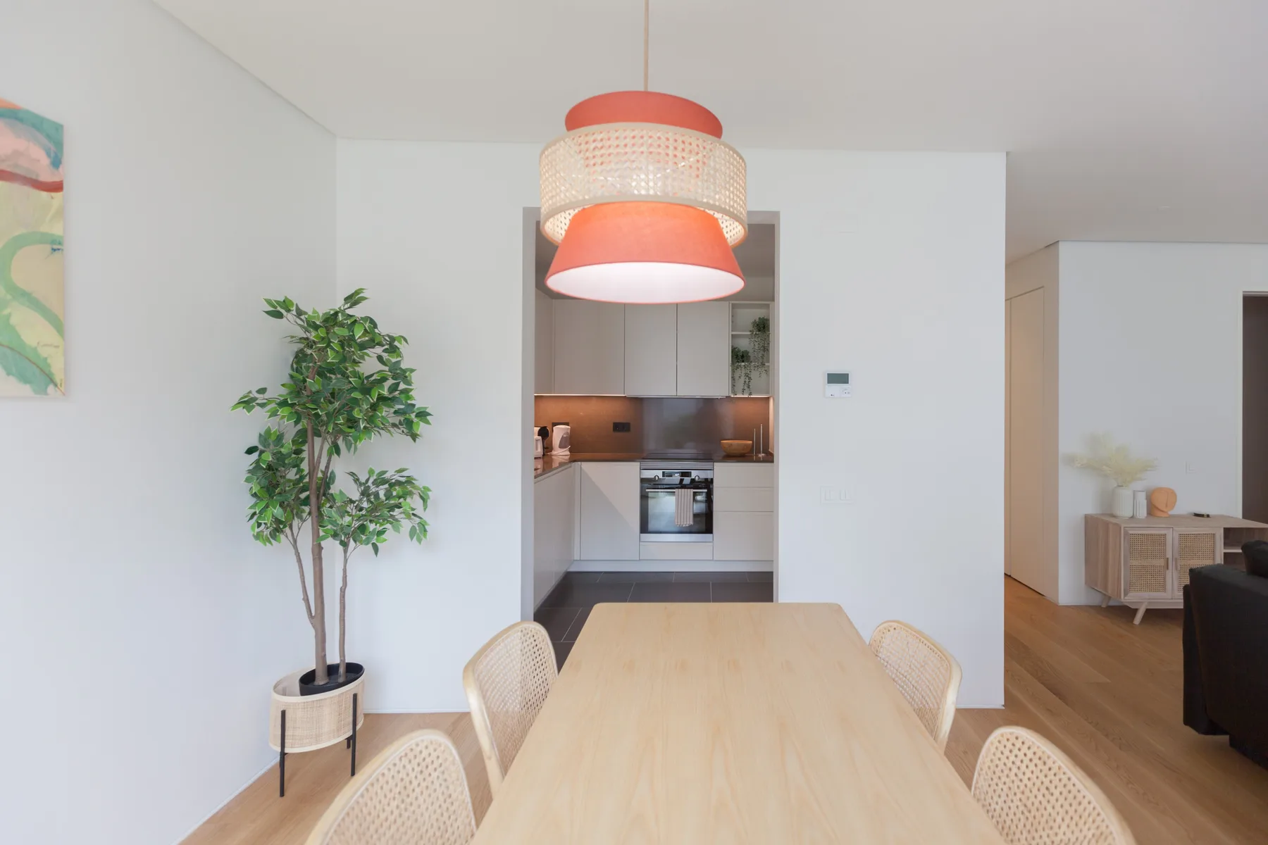 A dining area with a long wooden table and an open kitchen in the background.