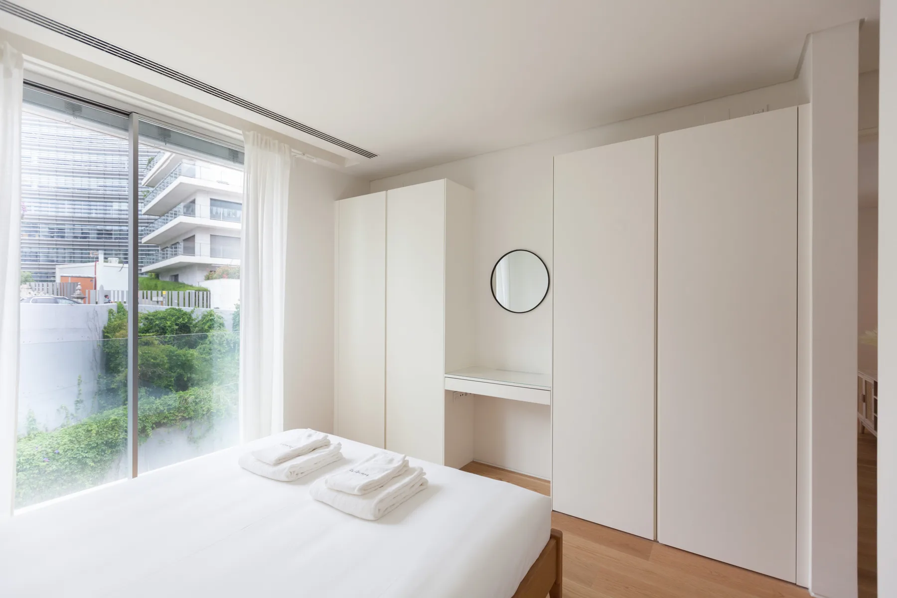 A bright bedroom with a bed beside floor-to-ceiling windows and built-in wardrobes.