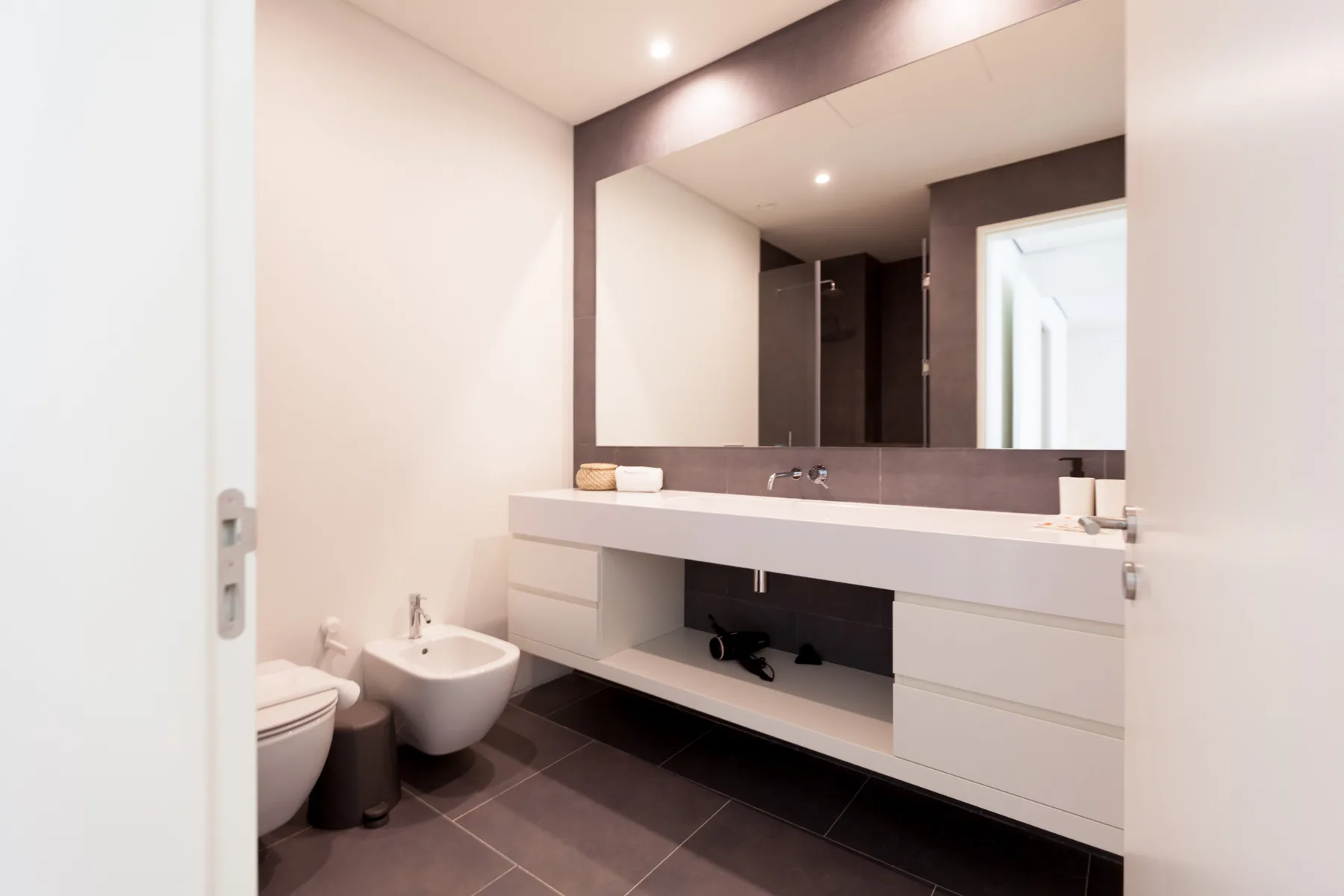 A modern bathroom with a wide sink vanity, mirror, toilet, and bidet.