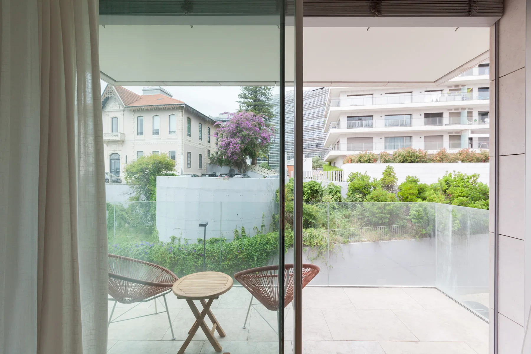 A bright living area opens onto a terrace with outdoor seating and greenery.