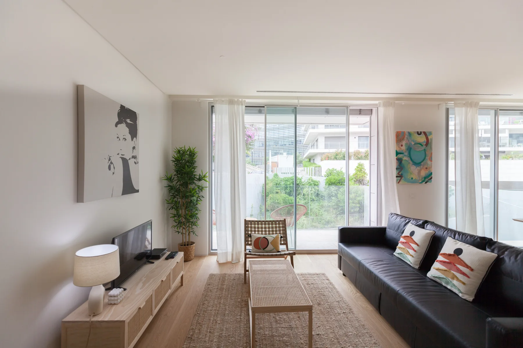 A bright living room with seating, a coffee table, and windows opening onto a balcony.
