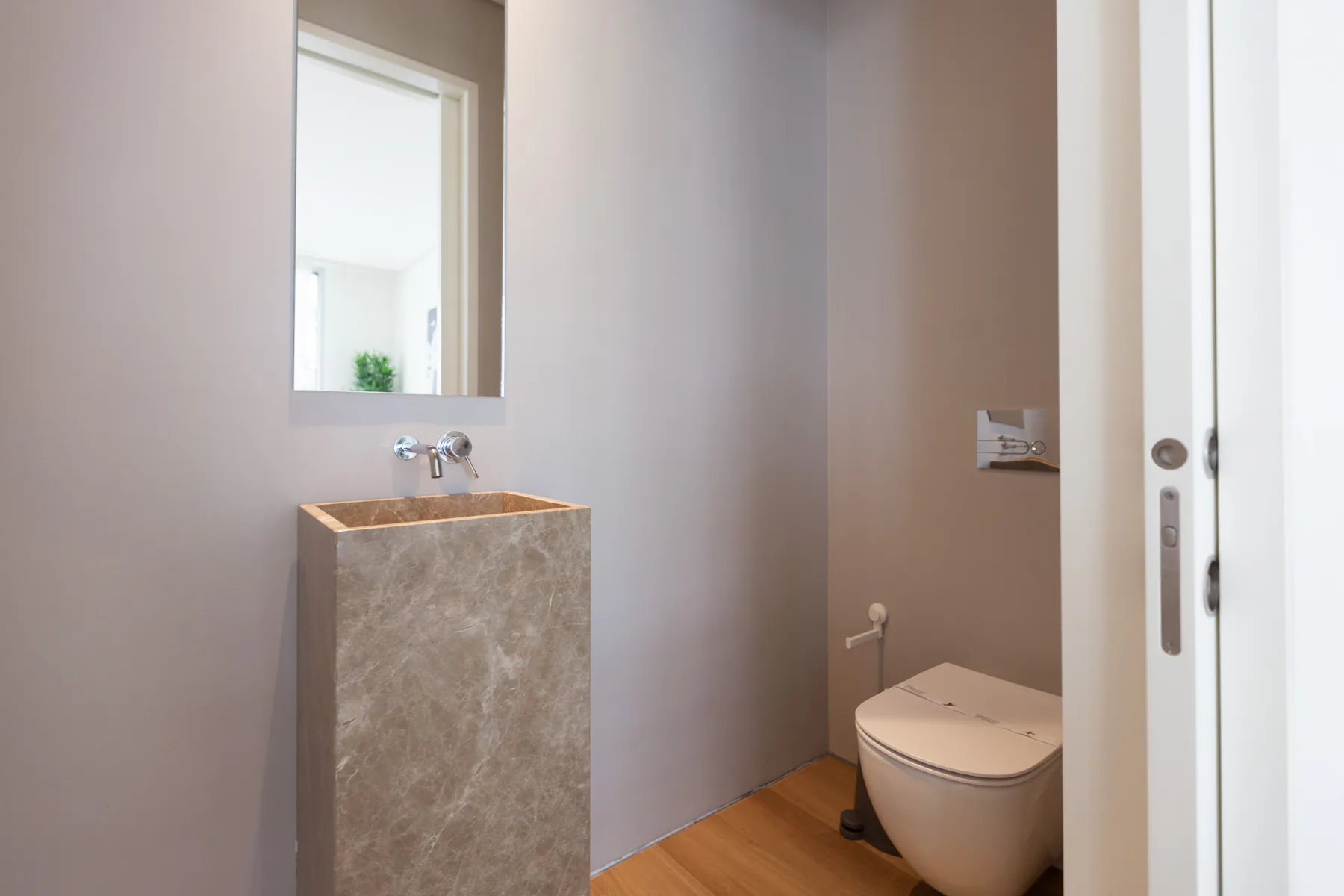 A bathroom with a stone-finished sink and toilet beside a white door.
