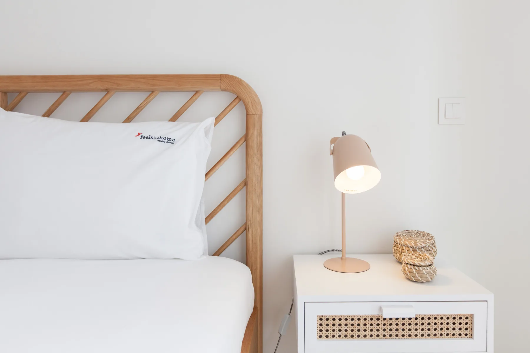 A bedroom with white bedding, a wooden headboard, and a bedside lamp.